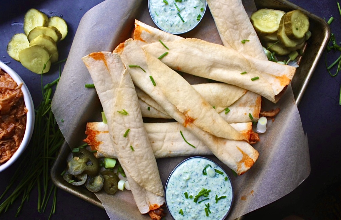 Sweet and spicy barbecue pulled chicken with caramelized onions and tons of spices all tucked into a warm, crisp oven baked tortilla: these Barbecue Chicken Taquitos with Herbed Crema are heavenly.