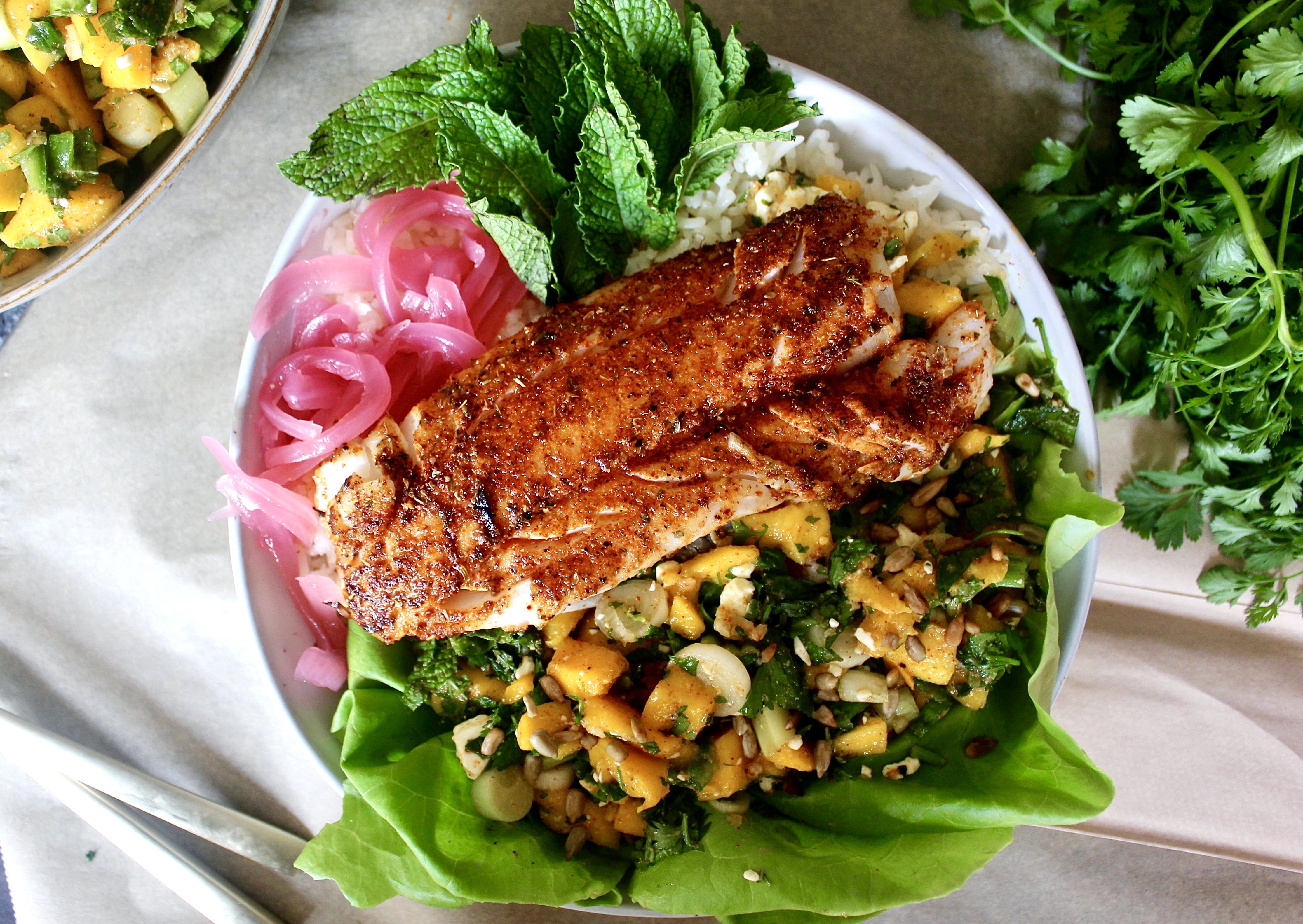 Spiced, crispy pan-seared fish with a sweet and spicy mango herb salad layered up over a bed of jasmine rice: these Mango Blackened Fish Taco Bowls are a game-changing dinner.