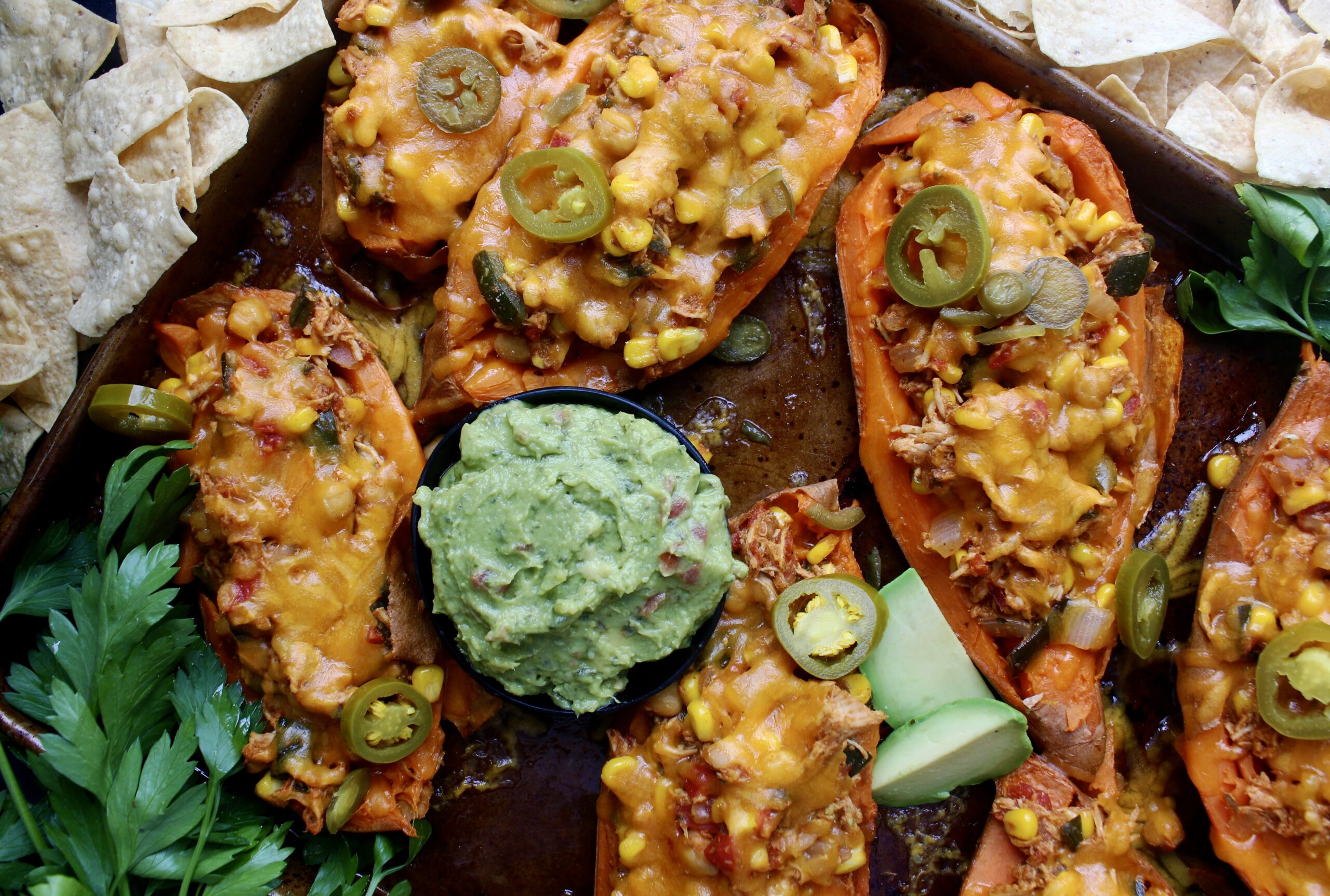 Juicy shredded chicken cooked down with seasoned corn, beans, peppers, and tomatoes all stuffed into a crispy sweet potato skin with tons of cheese: these Mexican Cheddar Stuffed Sweet Potato Skins are the ultimate fiesta food.