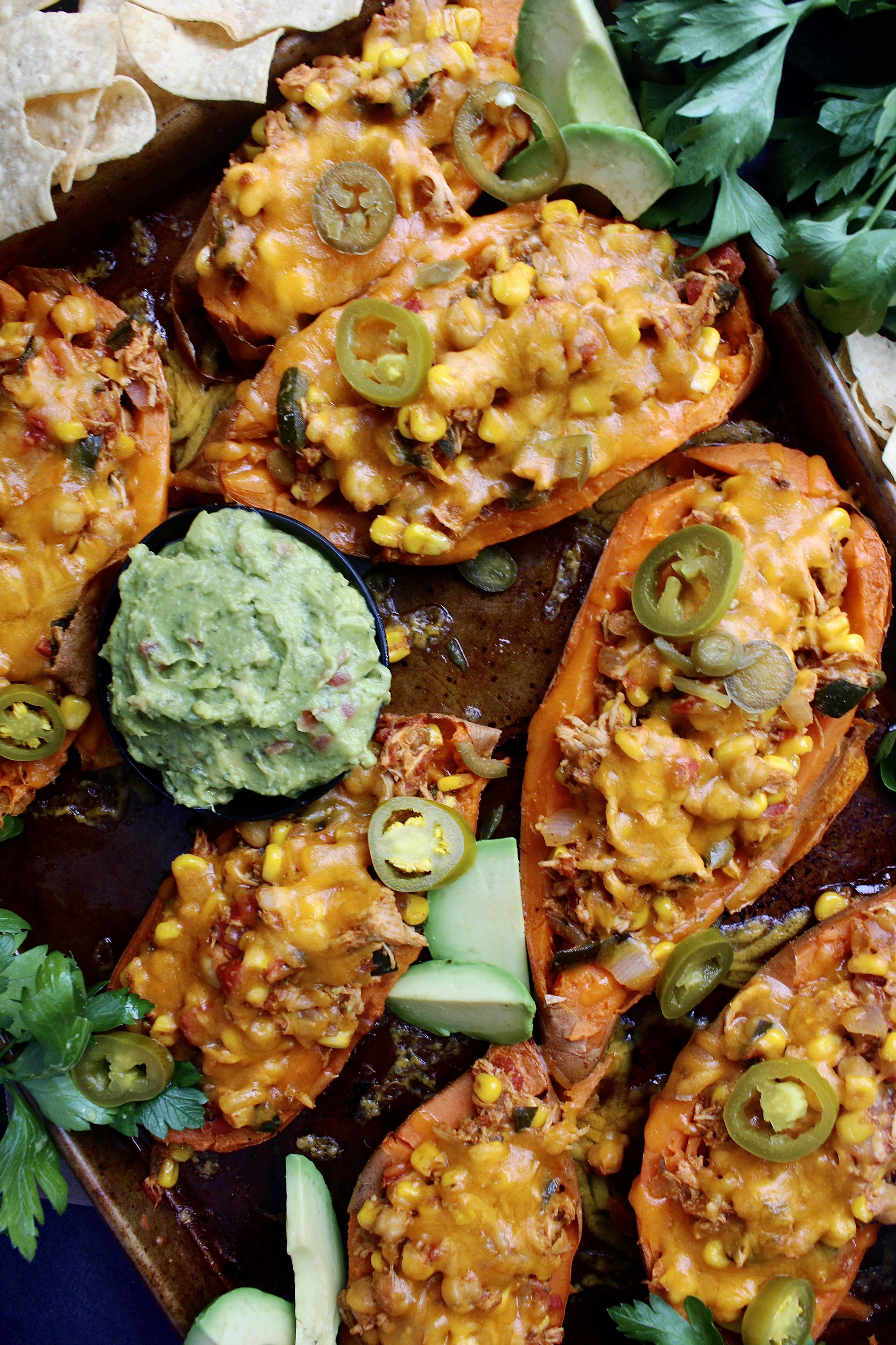 Juicy shredded chicken cooked down with seasoned corn, beans, peppers, and tomatoes all stuffed into a crispy sweet potato skin with tons of cheese: these Mexican Cheddar Stuffed Sweet Potato Skins are the ultimate fiesta food.