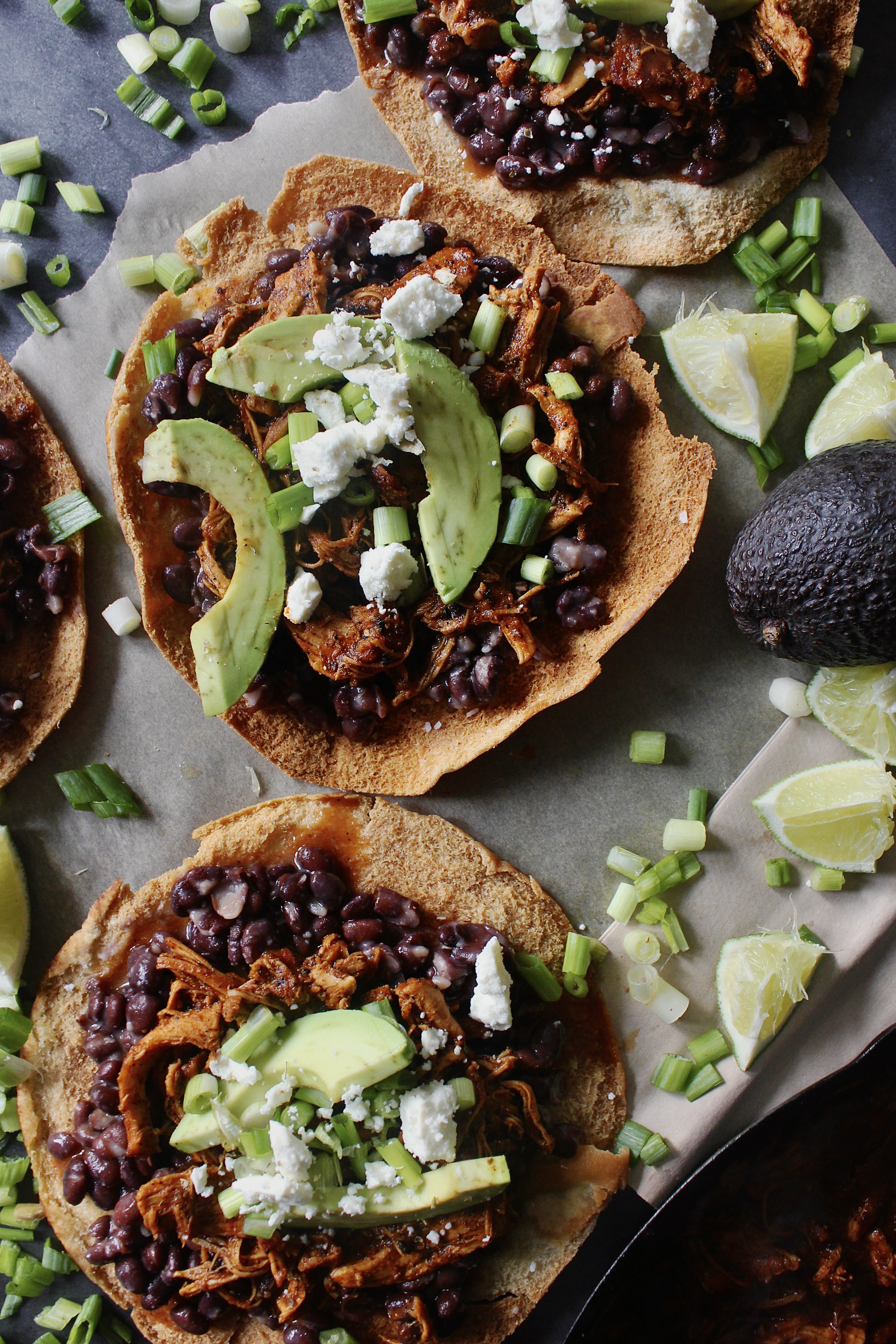 With juicy, spiced pulled chicken and tons of fresh flavors layered over a homemade crispy pita shell: these Chicken, Bean, Avocado, and Feta Pita Tostadas are the messy goodness that we all need right now!