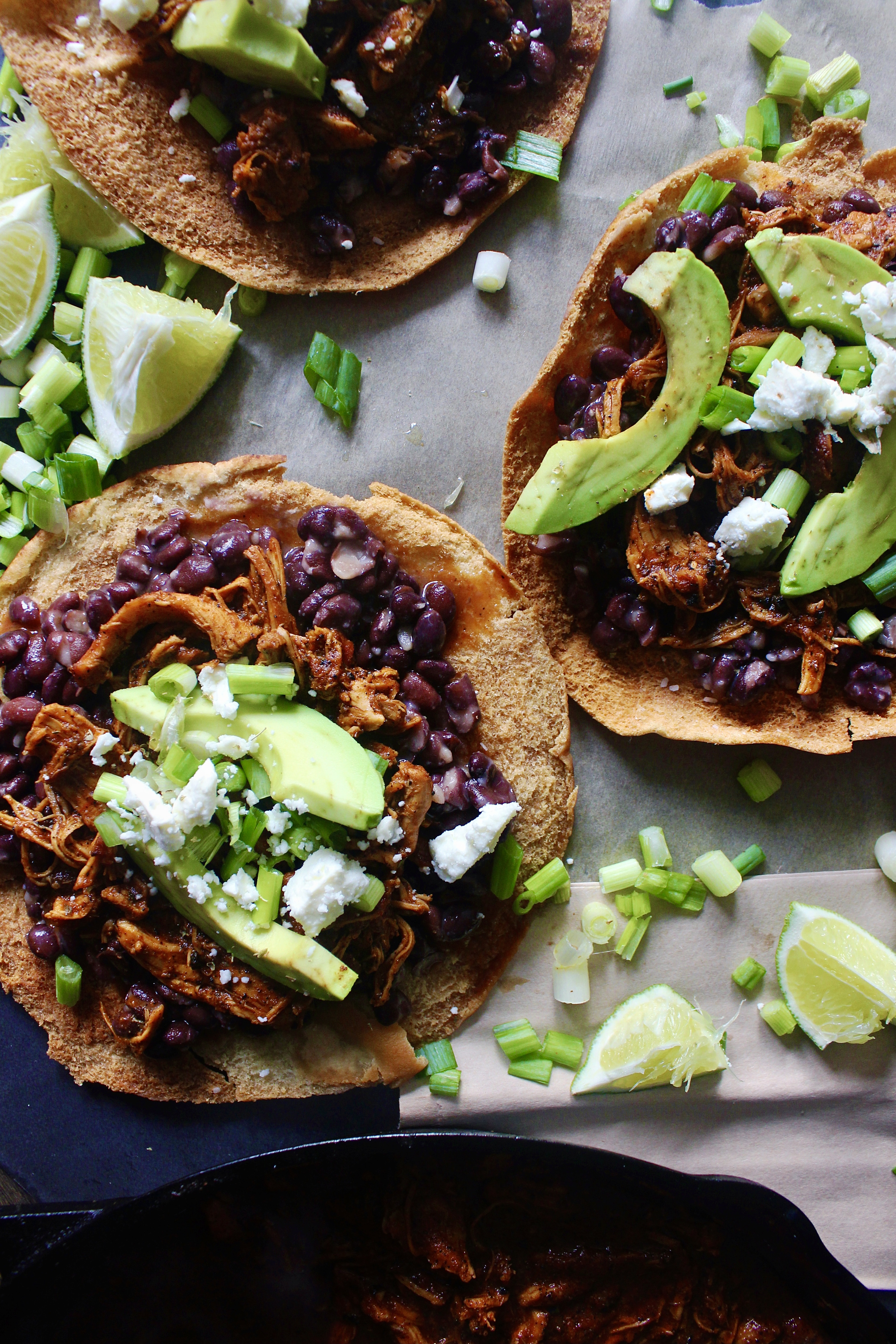 With juicy, spiced pulled chicken and tons of fresh flavors layered over a homemade crispy pita shell: these Chicken, Bean, Avocado, and Feta Pita Tostadas are the messy goodness that we all need right now!