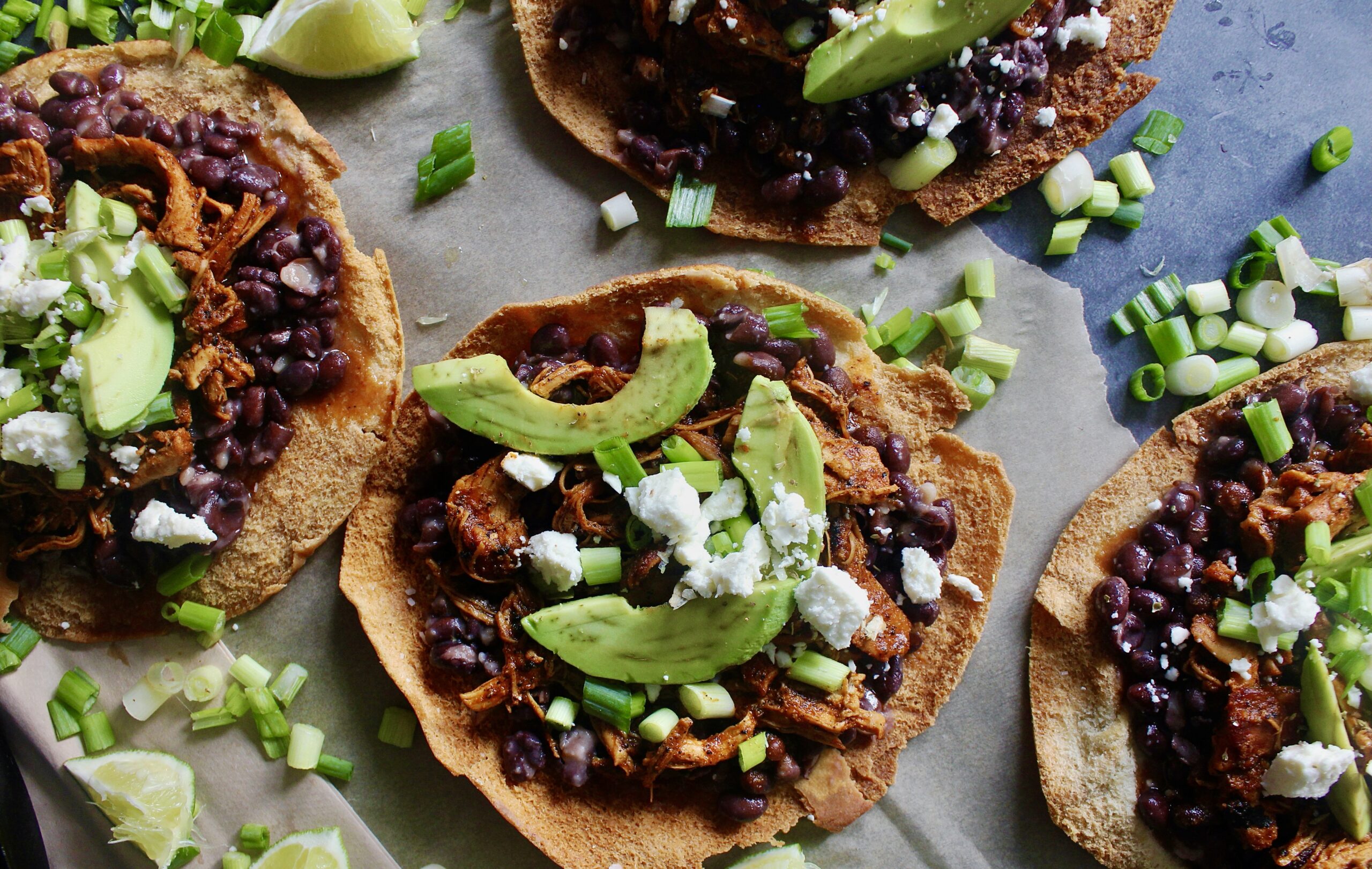 With juicy, spiced pulled chicken and tons of fresh flavors layered over a homemade crispy pita shell: these Chicken, Bean, Avocado, and Feta Pita Tostadas are the messy goodness that we all need right now!