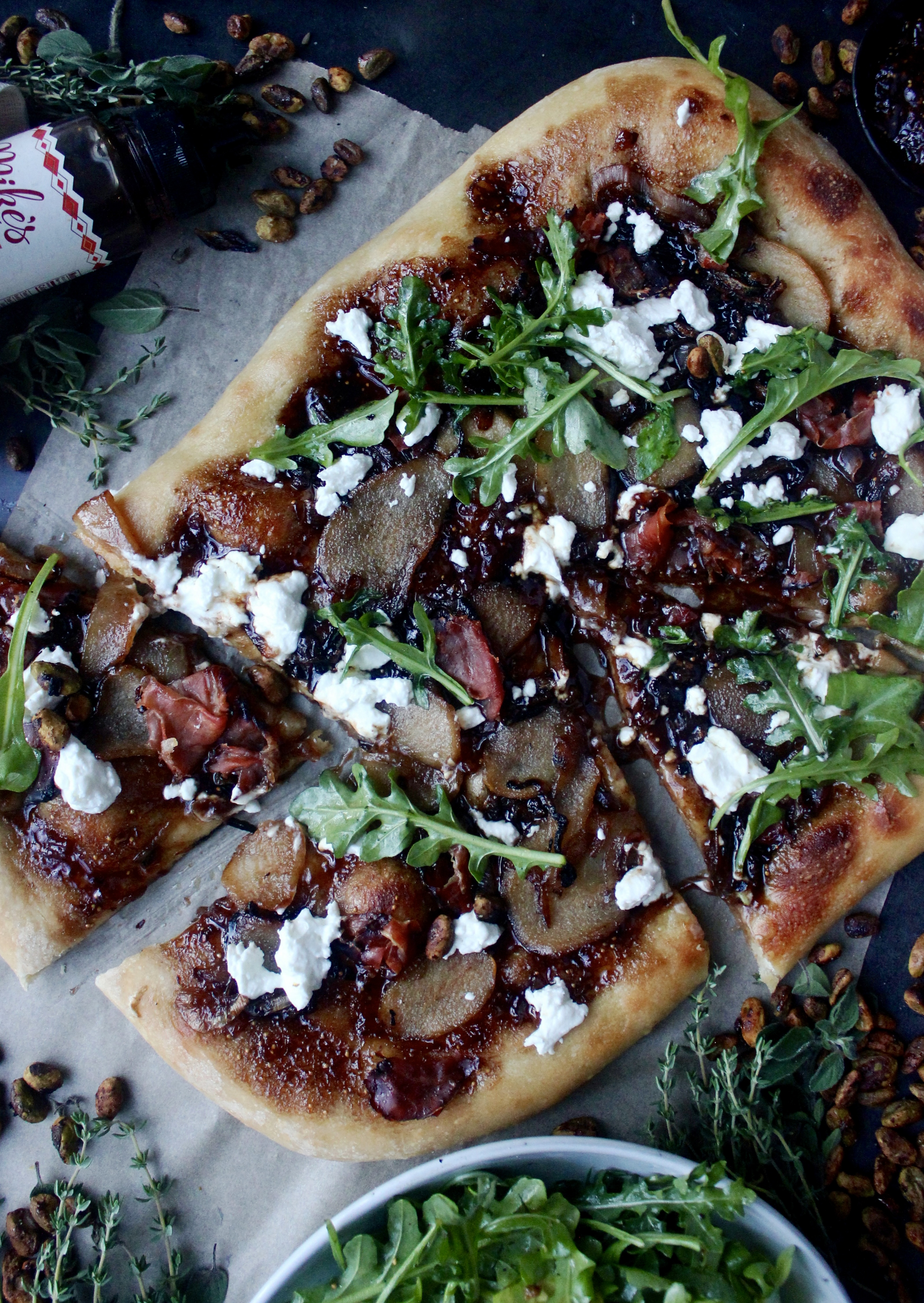 A warm, fluffy oven baked pizza layered with a jammy balsamic fig spread, honey caramelized pears, salty prosciutto, and melty goat cheese all topped off with a pistachio arugula salad: this Balsamic Caramelized Pear, Fig, and Prosciutto Pizza could not get any better.