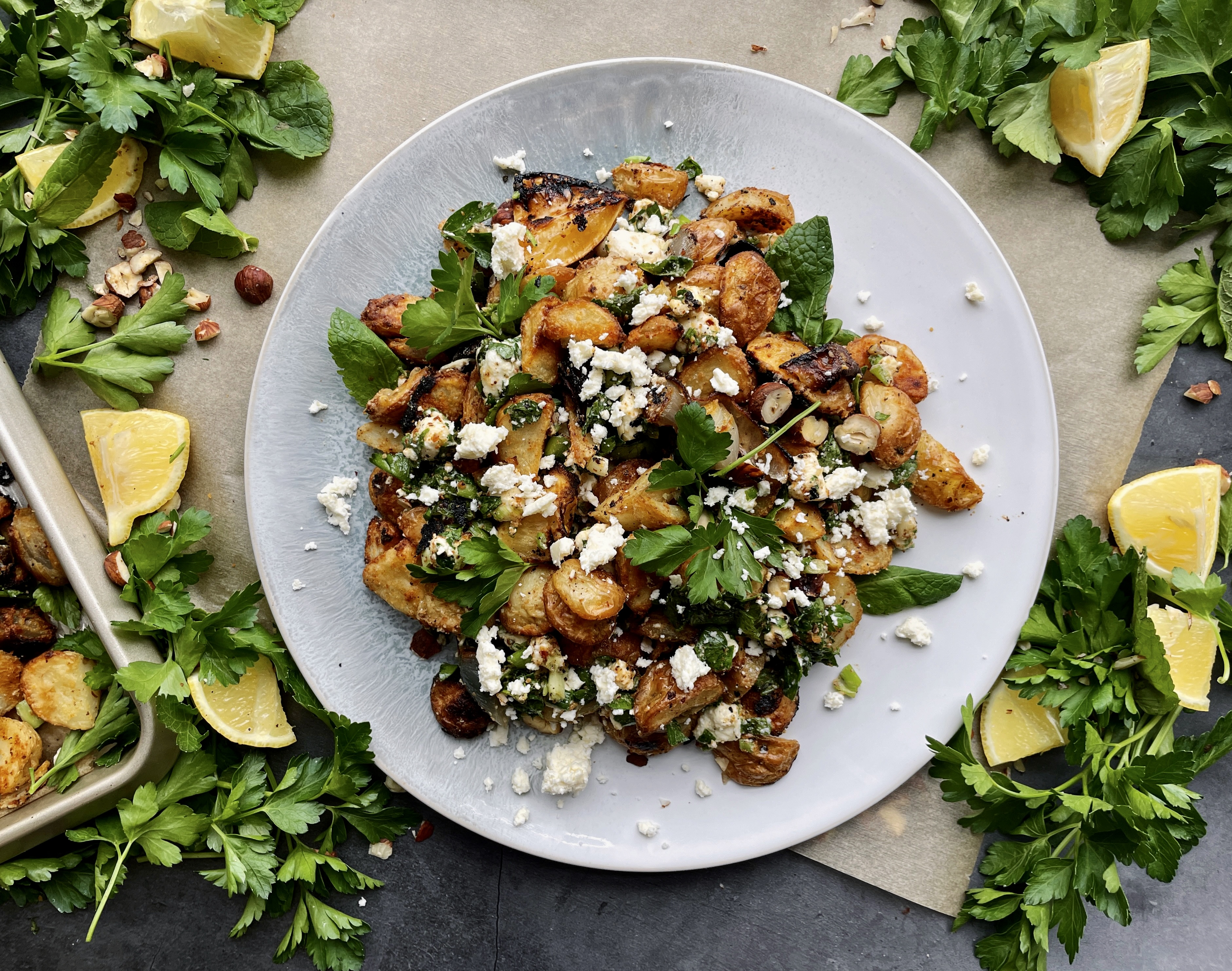 Roasted lemon, caramelized shallots, and your favorite hummus roasted up with baby potatoes and topped with allll the herbs and feta: these Crispy Greek Hummus Crusted Potatoes are an all time fav side!