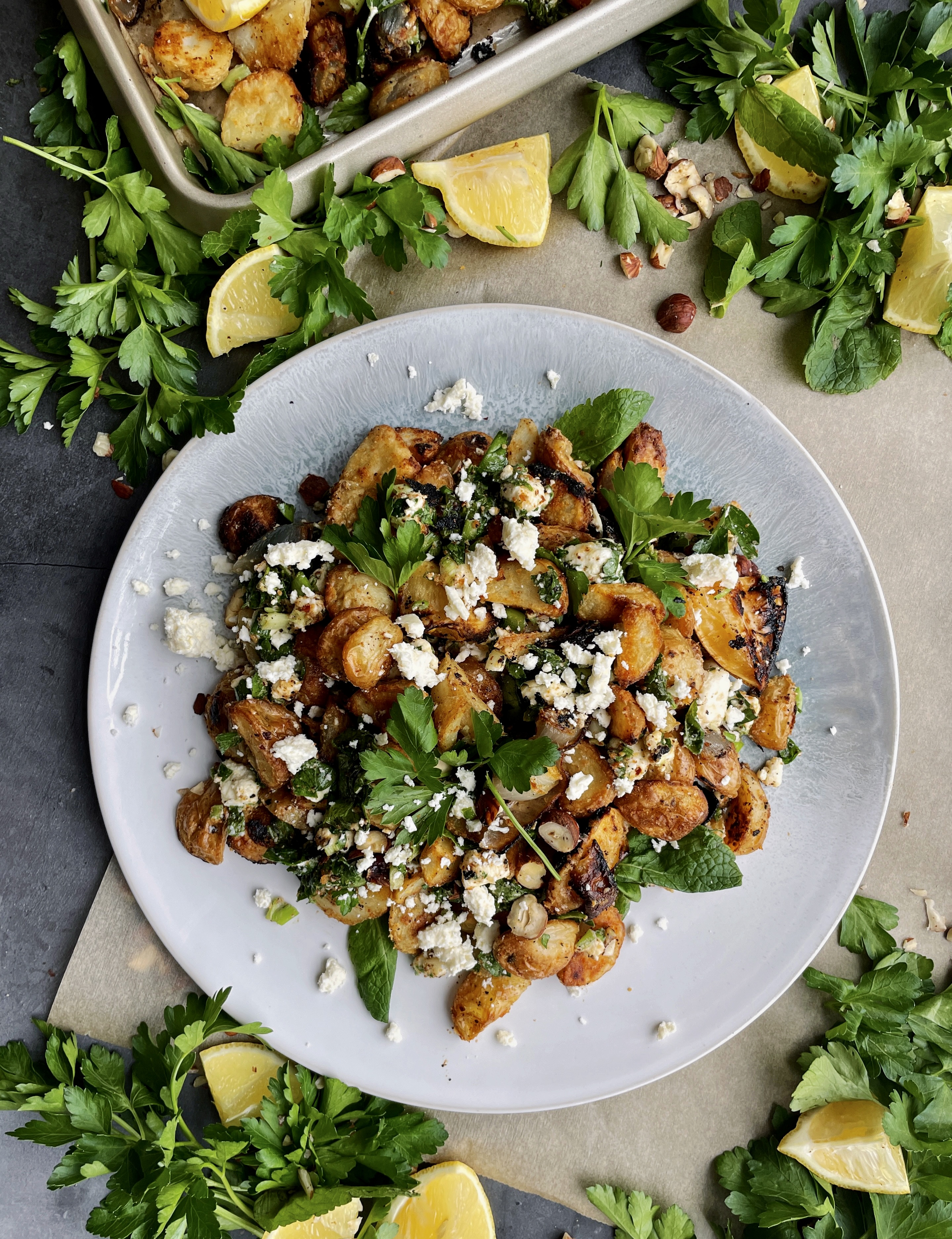 Roasted lemon, caramelized shallots, and your favorite hummus roasted up with baby potatoes and topped with allll the herbs and feta: these Crispy Greek Hummus Crusted Potatoes are an all time fav side!