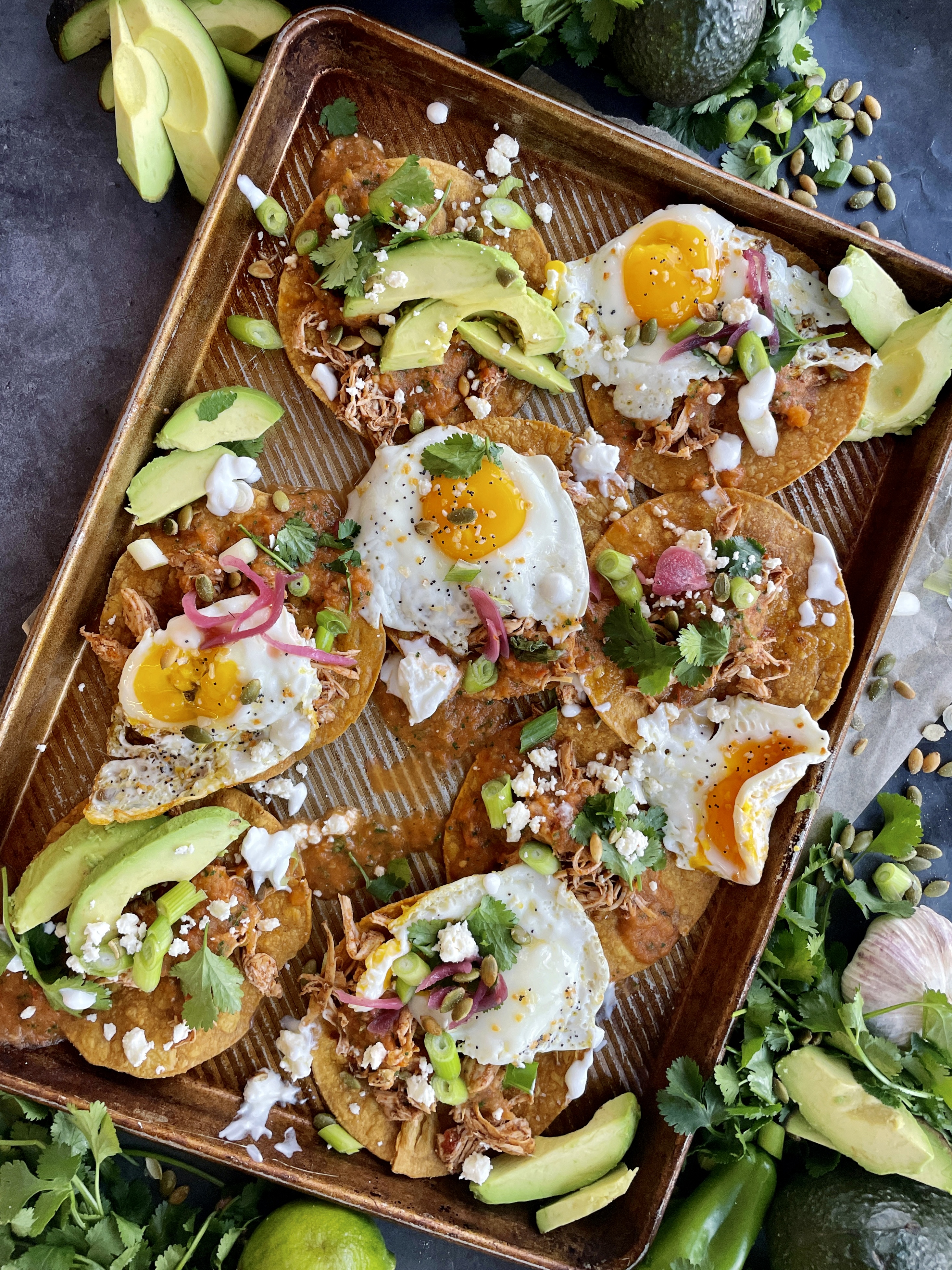 Crispy baked corn tortilla shells covered in the easiest smoky roasted salsa roja all topped off with fried eggs, cotija cheese, avocado, and all the bright flavors: these Baked Sheet Pan Tostada Chilaquiles are good any time of the day!!