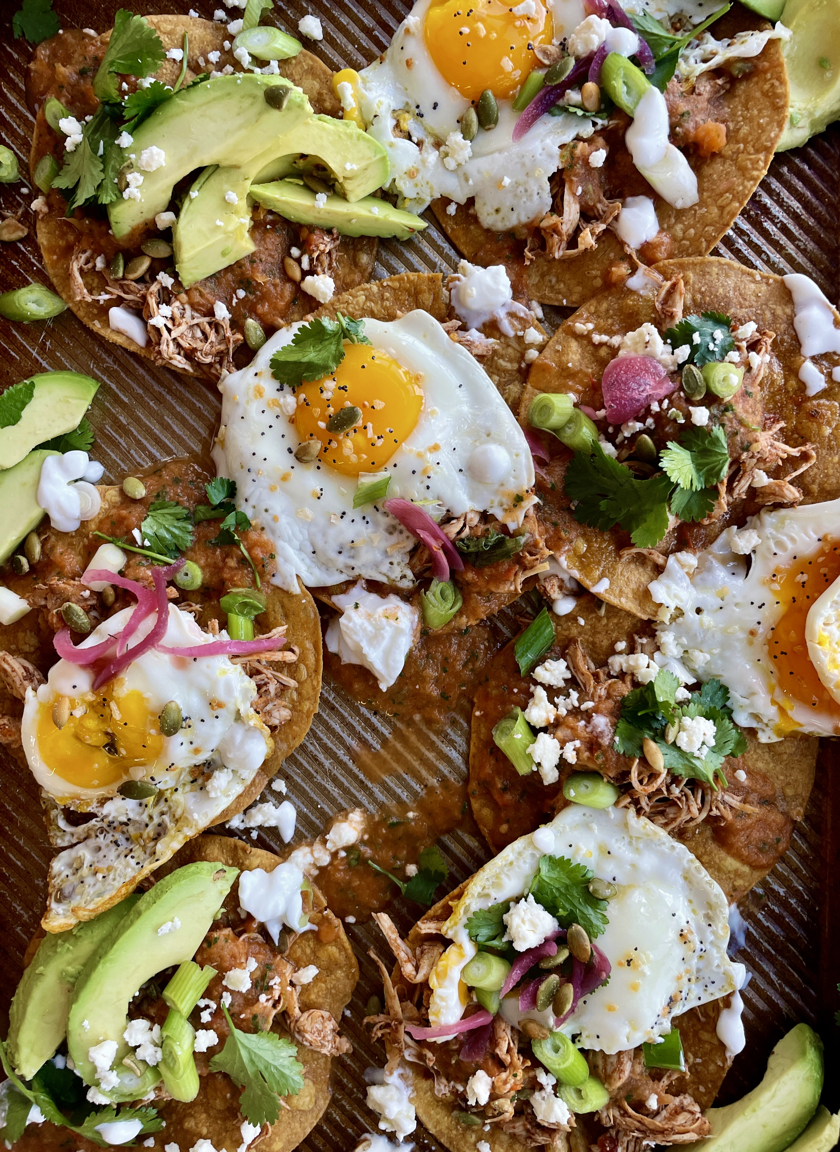 Crispy baked corn tortilla shells covered in the easiest smoky roasted salsa roja all topped off with fried eggs, cotija cheese, avocado, and all the bright flavors: these Baked Sheet Pan Tostada Chilaquiles are good any time of the day!!