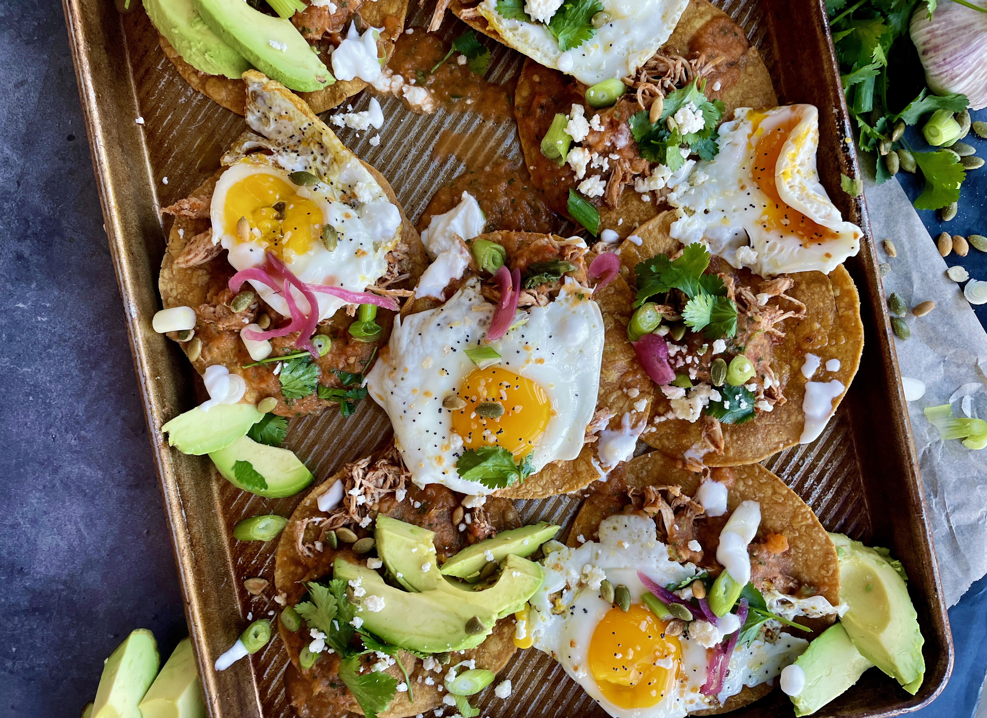 Crispy baked corn tortilla shells covered in the easiest smoky roasted salsa roja all topped off with fried eggs, cotija cheese, avocado, and all the bright flavors: these Baked Sheet Pan Tostada Chilaquiles are good any time of the day!!