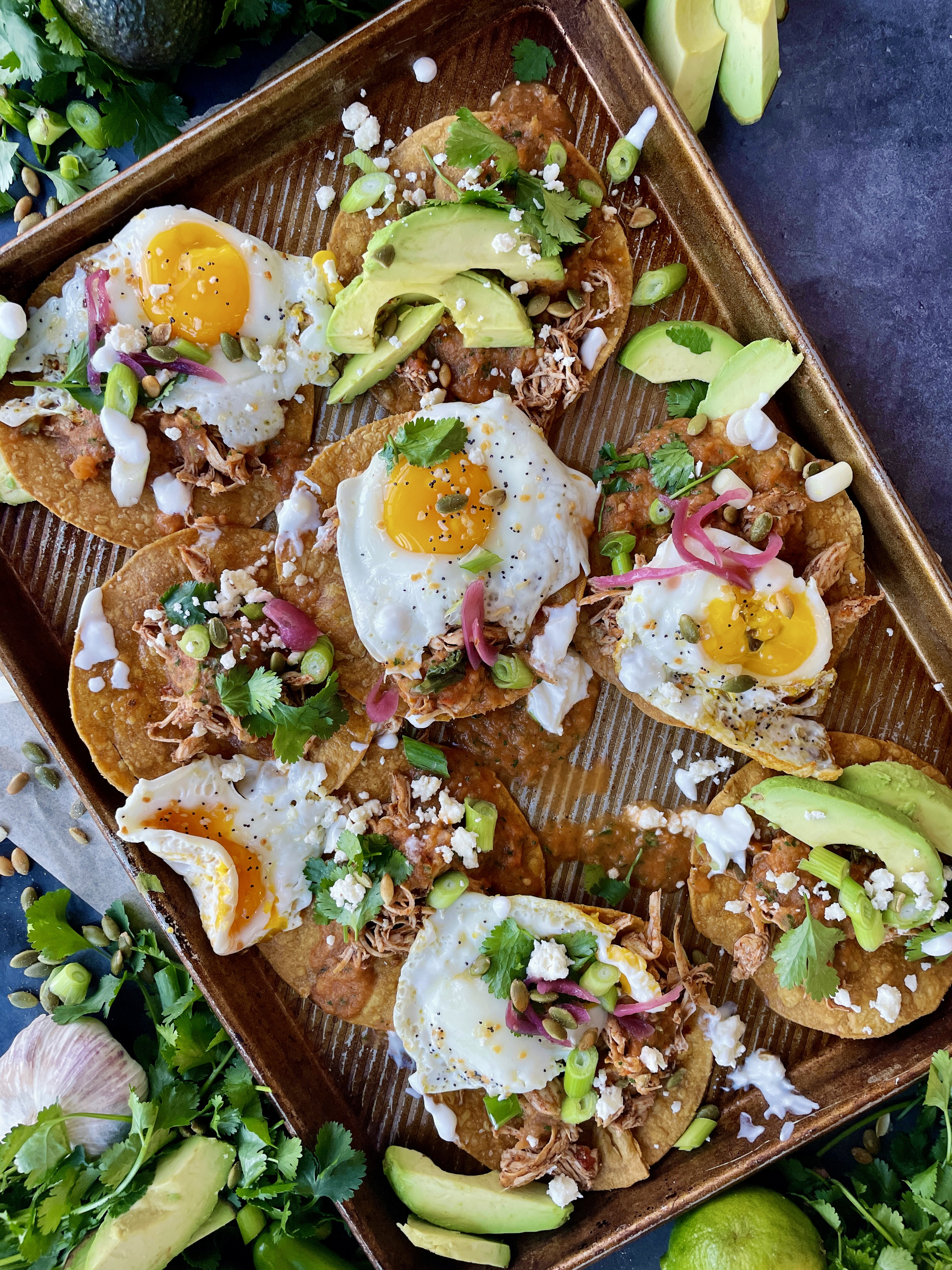 Crispy baked corn tortilla shells covered in the easiest smoky roasted salsa roja all topped off with fried eggs, cotija cheese, avocado, and all the bright flavors: these Baked Sheet Pan Tostada Chilaquiles are good any time of the day!!